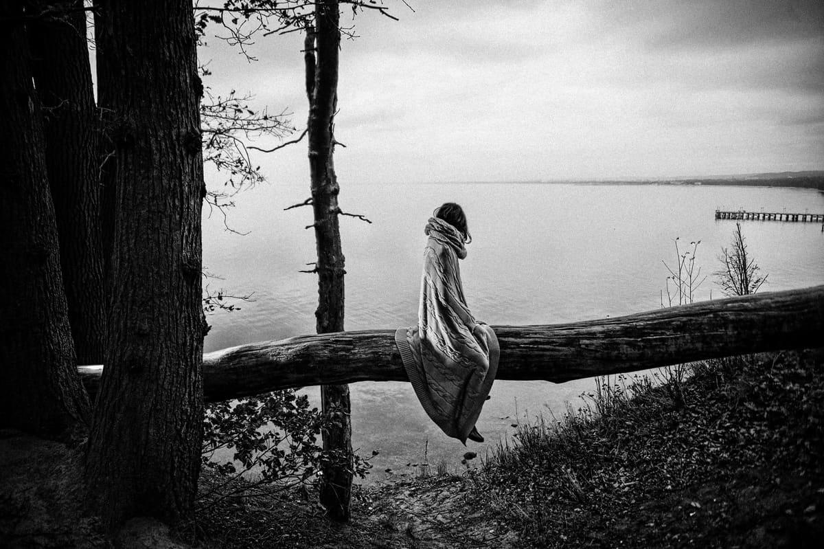 A woman siting on a dead tree, alone in the forest